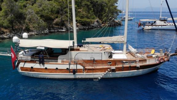 Die luxuriöse Gulet Cemre Mila ankert in einer ruhigen Bucht, umgeben von türkisfarbenem Wasser und bewaldeten Hügeln.