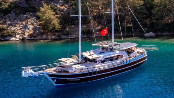 The luxurious Gulet yacht anchored in a serene, pine-lined bay in Fethiye.