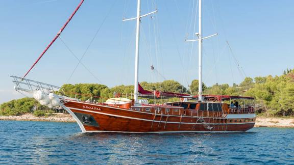 The gulet Croatia, with its wooden hull and spacious deck, is peacefully anchored in the open sea.