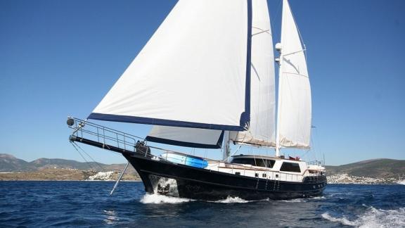 Sailing yacht with white sails and black hull sails in the sunshine.