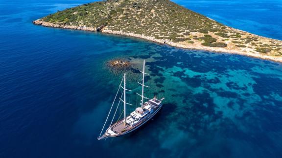 Ein Gulet in Bodrum liegt in ruhigem, kristallklarem Wasser vor einer grünen, felsigen Inselküste.