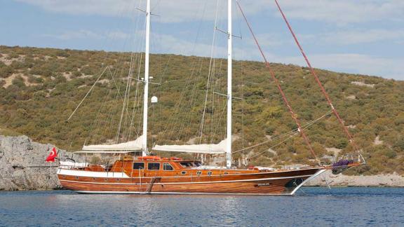 A classic, wooden gulet with two masts, anchored on a quiet shore in Bodrum.