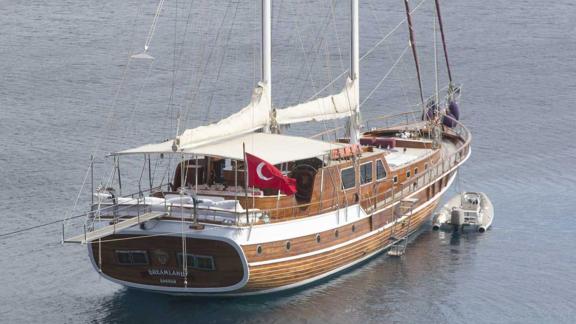 A traditional wooden gulet flying the Turkish flag, anchored in a quiet spot in clear waters.