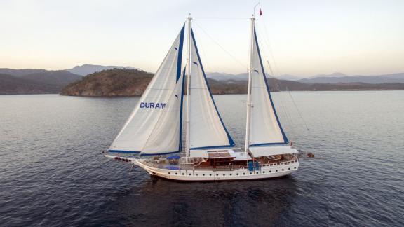 Luxurious gulet Duramaz with 6 cabins on calm waters in Fethiye, surrounded by picturesque coastal scenery.