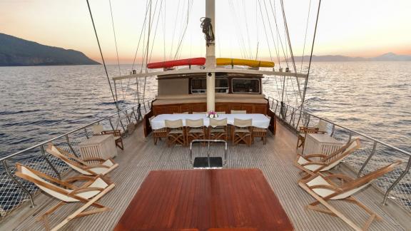 The deck of the Gulet Efe Burak with dining area and lounge chairs at sunset.