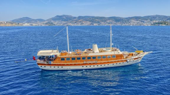 An elegant wooden sailing ship on the open sea with mountains in the background.