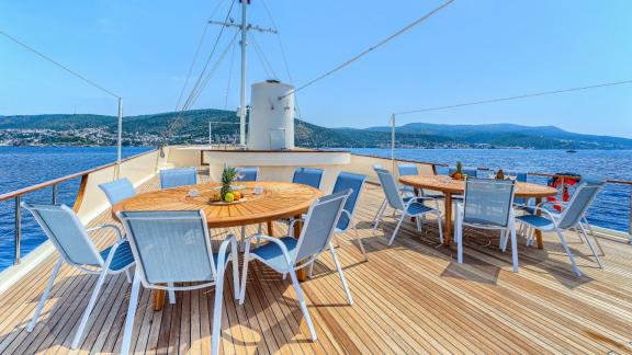 Upper deck of the Elara 1 with round tables, blue chairs and breathtaking sea views