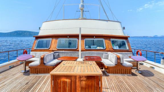 Deck of the Elara 1 with wooden furniture and seating areas, surrounded by sea and clear skies.