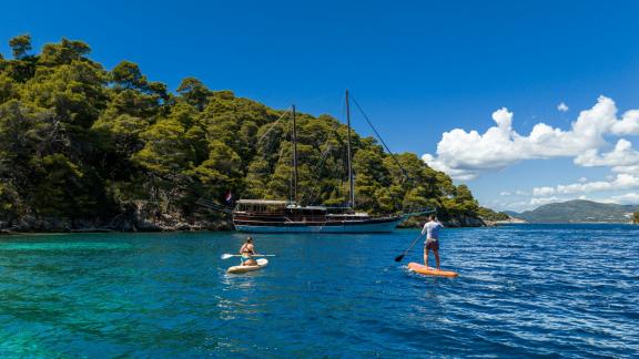 Gäste paddeln vor der vor Anker liegenden Gulet Eleganza in einer malerischen Bucht bei Split.