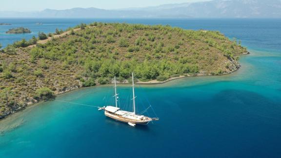 Die Yacht Enderim A ankert in einer abgeschiedenen Bucht mit türkisfarbenem Wasser und grüner Landschaft.