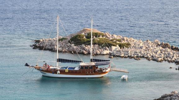 The Gulet Erden anchored in a tranquil cove with rocks and clear water.