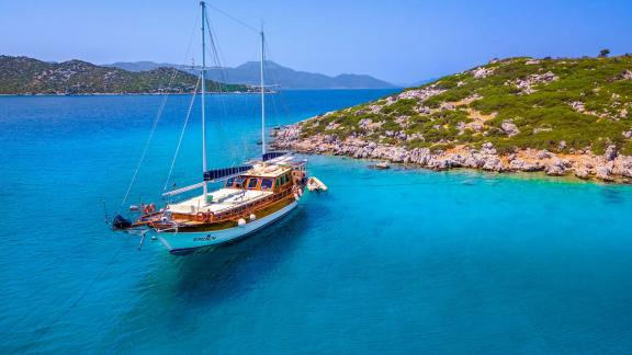 Die Gulet Erden liegt in einer malerischen, türkisblauen Bucht vor Anker, umgeben von grünen Hügeln und Felsen.