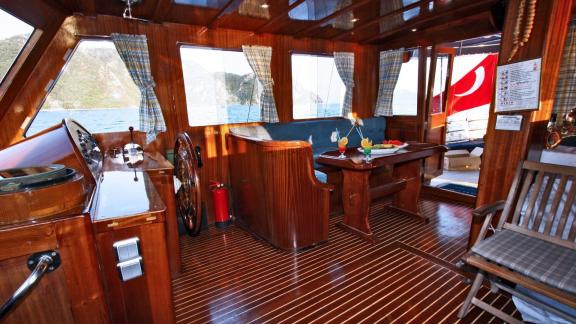 Cozy interior of Gulet Erden with wooden furniture, seating area, helm, and windows with a sea view.