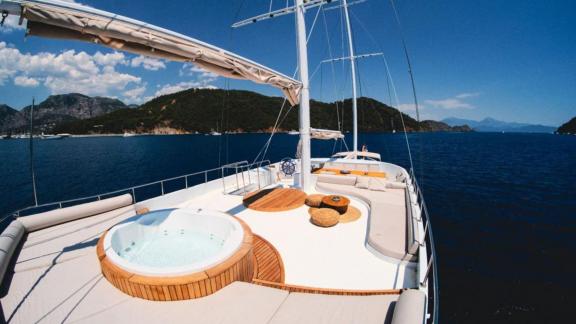 A whirlpool and seating area on the deck of a gulet, surrounded by a picturesque coastal landscape.