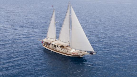 Elegant 4-cabin gulet with full sails, sailing on calm sea.