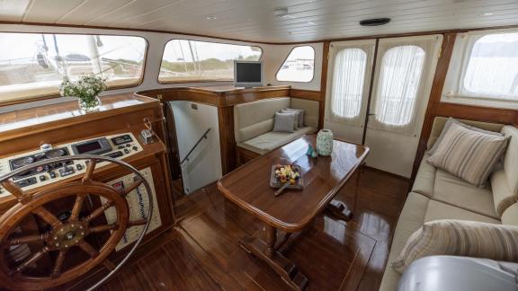 The gulet's helm with wooden wheel, dining table, and cozy sofas.