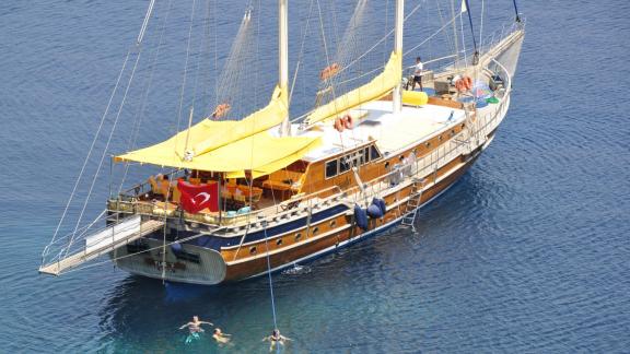 Bodrum-Gulet Flas VII mit ihren 8 Kabinen, wie sie ruhig im klaren Wasser vor Anker liegt. Menschen genießen das Wasser