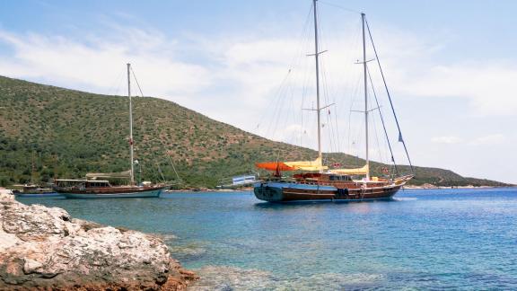 Die Bodrum-Gulet Flas VII liegt in einer malerischen Bucht vor Anker, umgeben von grünen Hügeln und klarem Wasser.