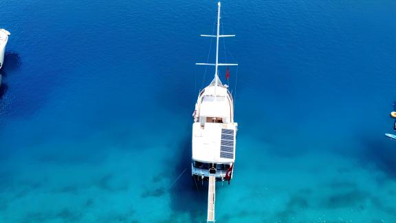 Aerial view of a sailing yacht anchored in clear, blue water.