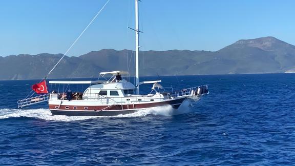 Sailing yacht with Turkish flag cruising on the sea with a mountain backdrop.