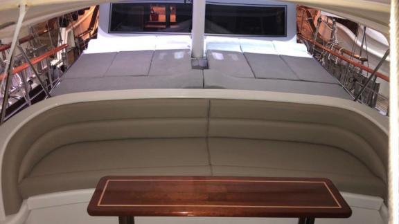 Cushioned seating area with a wooden table and sun loungers on a yacht deck.