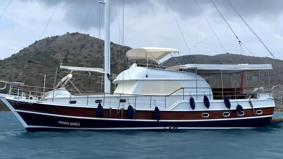 Side view of a sailing yacht docked in a harbor with a mountain backdrop.