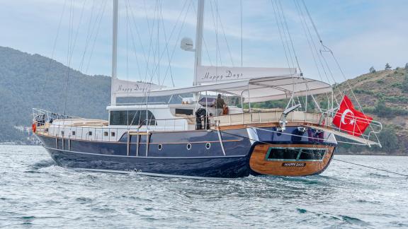 In Fethiye gulet charter option Happy Days cruising with side view and flag at stern visible.