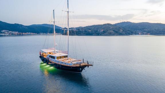 In Fethiye gulet charter option Happy Days anchored at sea in evening with lights on visible.