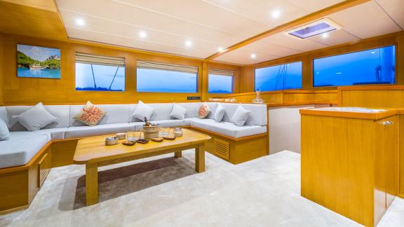 In Fethiye gulet charter option Happy Days interior salon with large seating area and table visible.