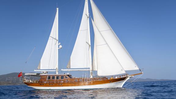 Elegant sailing yacht with white sail and classic wooden hull off the coast of Bodrum on a sunny day.