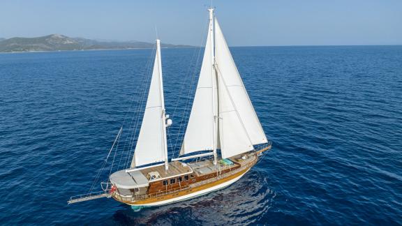 Wooden sailing yacht with white sails off the coast of Bodrum on a clear, sunny day.