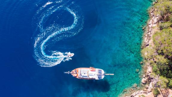 Die Gulet Cetin ankert in einer türkisfarbenen Bucht, während ein Beiboot eine Schleife im Wasser zieht.