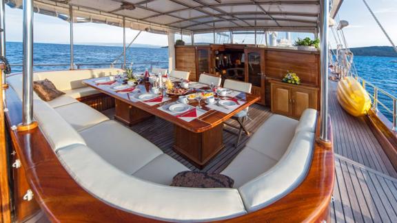 Set dining table on the deck of a gulet, surrounded by a cosy bench and calm sea.