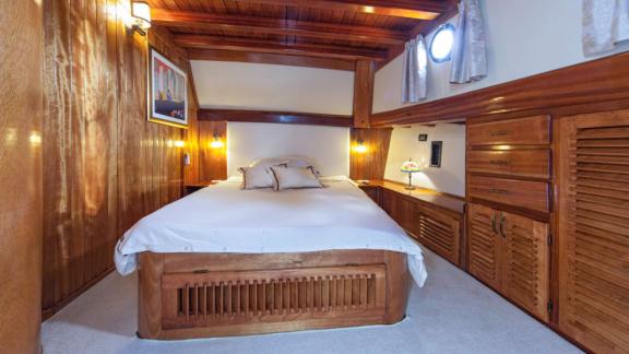 Cosy bedroom on a gulet with wooden interior and double bed, illuminated by soft light.