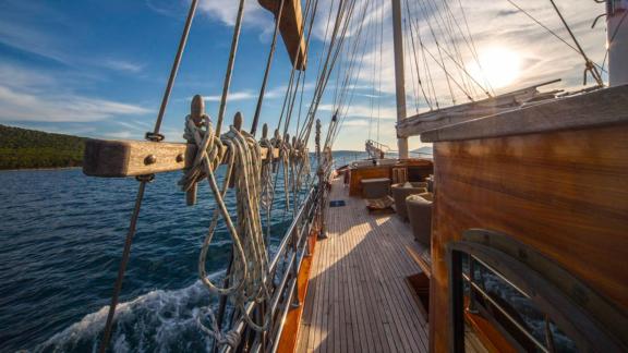 Side view of a gulet at sunset with ropes and deck details, sailing on a calm sea.