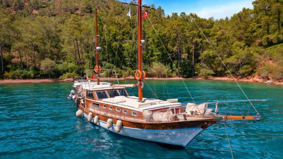 The Gulet Lina 2 anchored in a tranquil cove with turquoise water, surrounded by green nature.