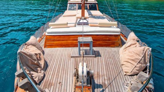 Foredeck of Gulet Lina 2 with sun loungers and cushions, surrounded by turquoise water.