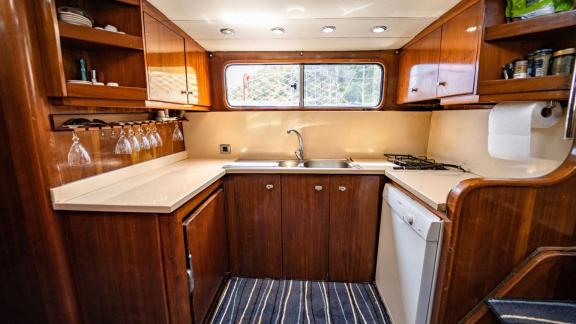 Compact galley of Gulet Lina 2 with wooden cabinets, sink, stove, and a window.