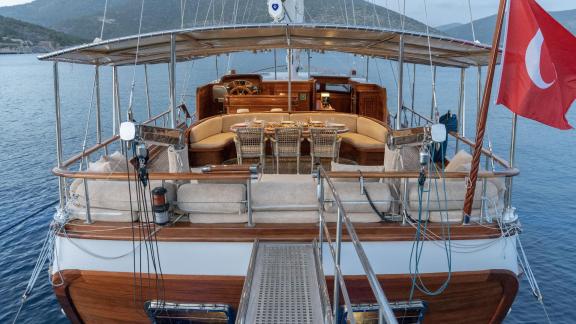 A view of the stern area of the gulet Lorient, with a cosy seating area and a dining table, at anchor in calm waters.