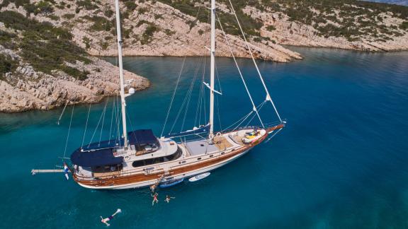 The gulet Lotus is anchored in the clear blue waters off a rocky coast in Croatia, surrounded by swimmers and water spor