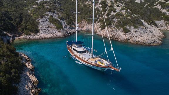 The gulet Lotus is anchored in a picturesque bay in Croatia, surrounded by clear blue waters and rocky coasts.