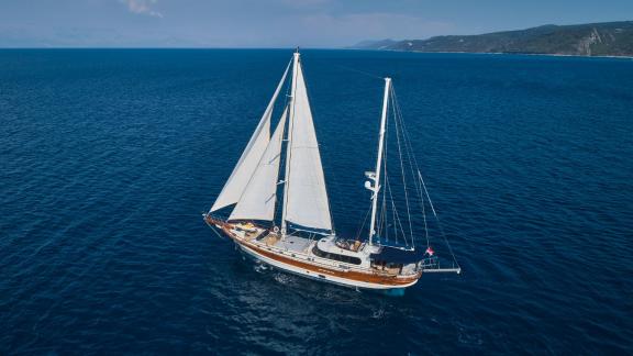 The gulet Lotus sails majestically across the open sea in Croatia, with full sails and a picturesque coastline in the ba