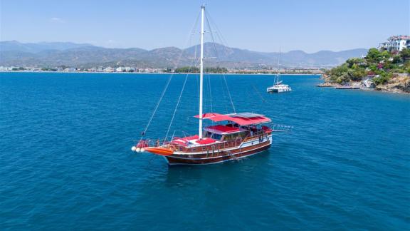 Die Gulet Lycian Sirius segelt auf dem blauen Meer vor Fethiye, im Hintergrund eine malerische Küste und Hügel.