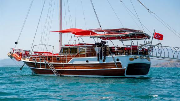 Die Gulet Lycian Sirius mit rotem Sonnenschutz liegt vor Anker im blauen Wasser vor Fethiye, die türkische Flagge weht i