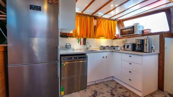 Kitchen of Gulet Lycian Sirius featuring a stainless steel refrigerator, dishwasher, coffee maker, and orange curtains.