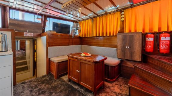 Interior of Gulet Lycian Sirius featuring a seating area, a small wooden table, a TV, and orange curtains.