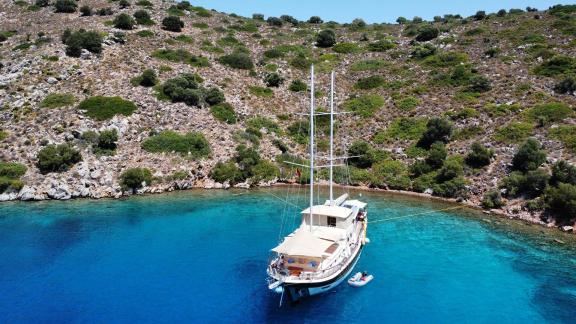 Die Charter Gulet Mare Magico liegt bei Marmaris in klarem Wasser vor Felsen, mit Tender am Heck.