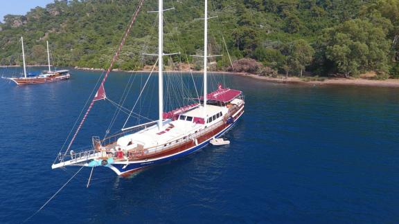 The Gulet Nirvana 2 is anchored in a serene bay with green hills and clear water.