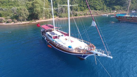 Die Gulet Nirvana 2 mit türkischer Flagge liegt vor Anker in einer Bucht mit grünen Hügeln und klarem Wasser.