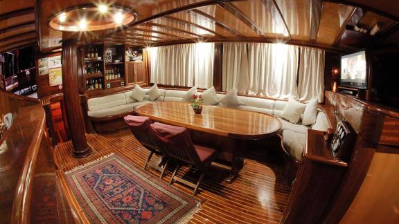 Luxurious interior of Gulet Nirvana 2 with dining table, lounge area, wooden walls, and TV.